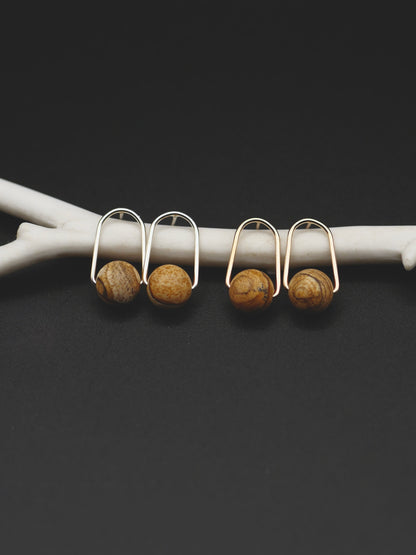 Two pairs of small earrings with round brown jasper beads, displayed on a white branch against a dark background.